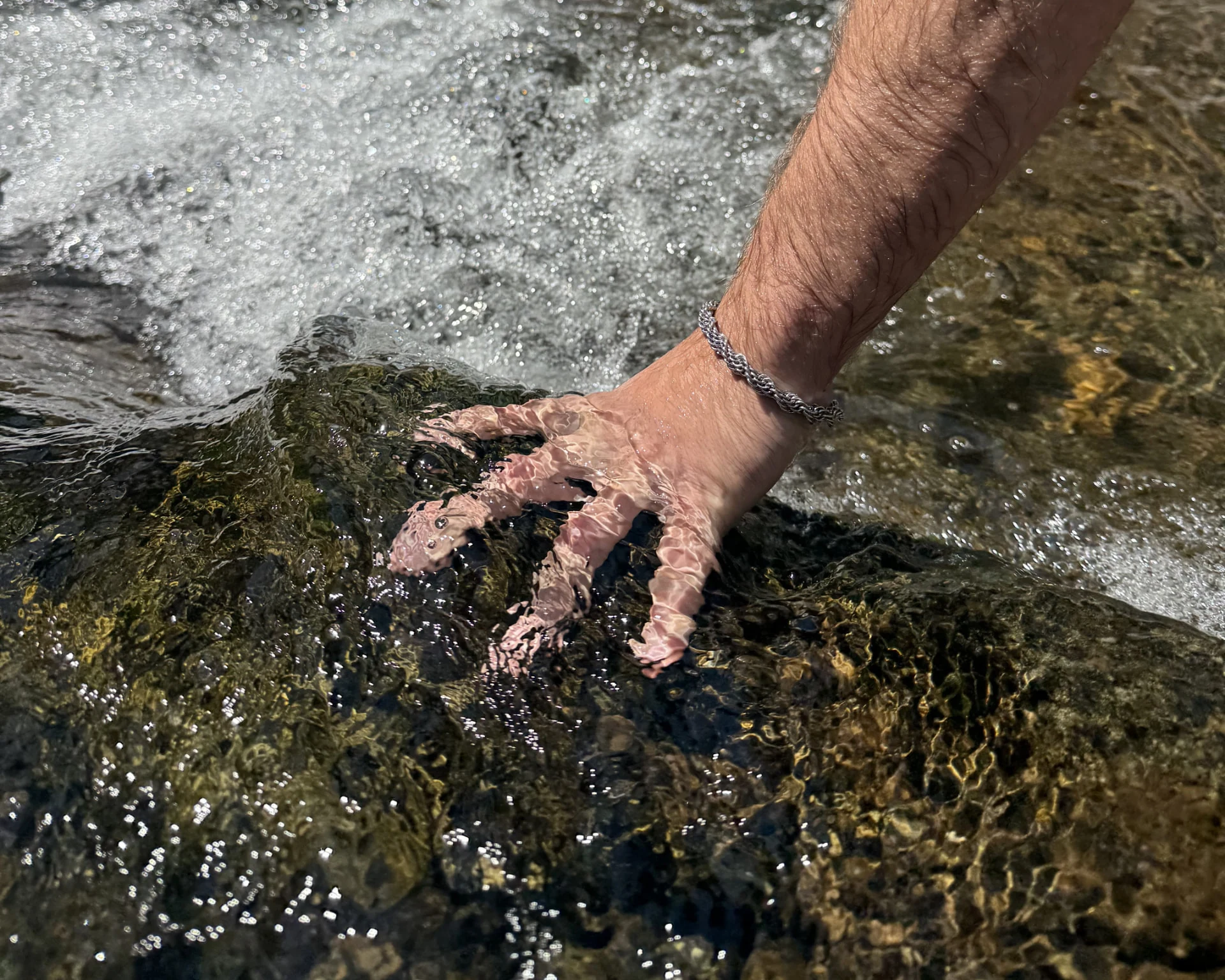 A hand wearing Steel Kloth reaches into rushing water